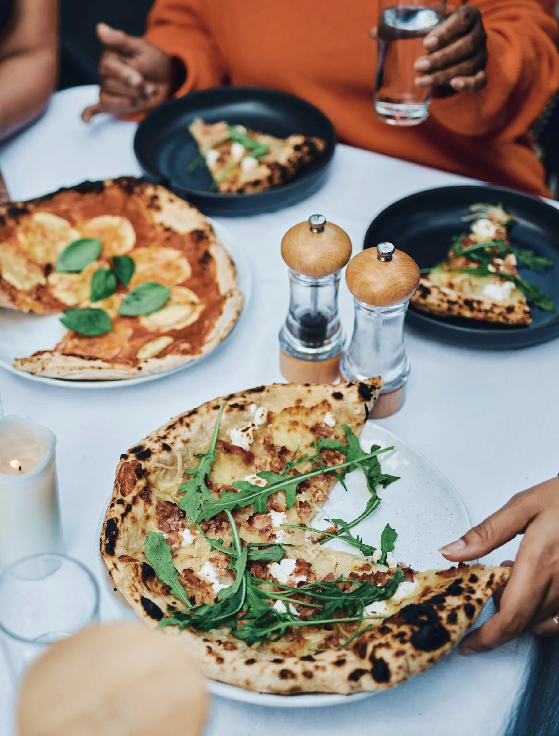 Friends sharing wood-fired pizzas around a candlelit table